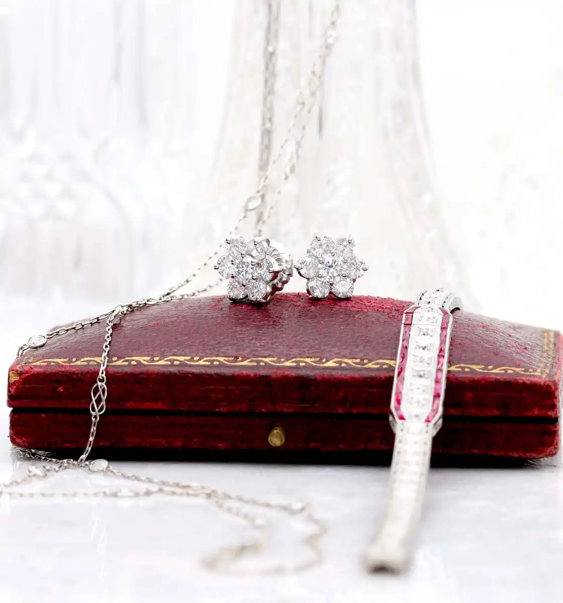 Diamond cluster stud earrings resting on a vintage red velvet jewelry box.