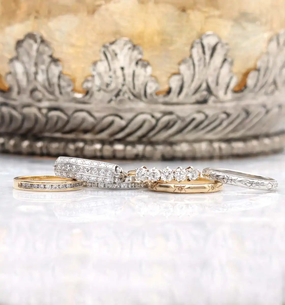 Ornate silver and gold rings with diamond accents arranged in front of a decorative crown.